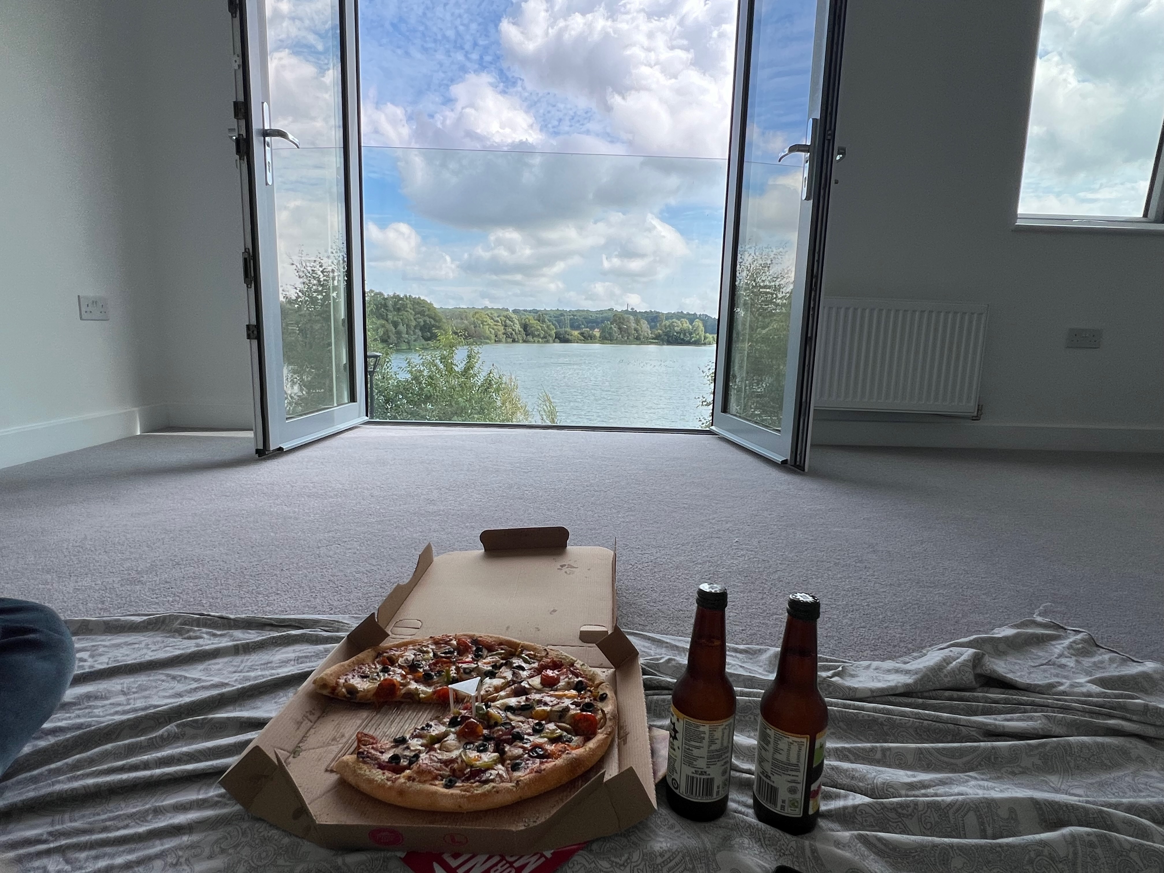 veg pizza and 2 bottles of fruit beer in front of door looking to blue sky and lake